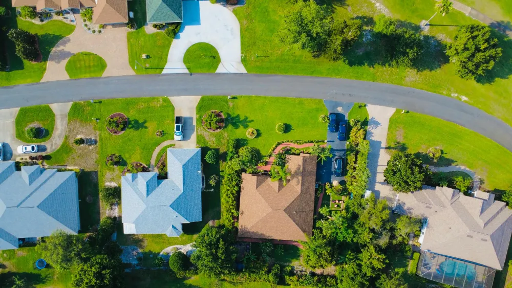 Overhead aerial drone photo of a suburban neighbourhood showing several homes, their driveways, landscaped lots, and the road curving between them. Top down real estate drone photography like this makes lot size and property boundaries immediately clear to buyers.